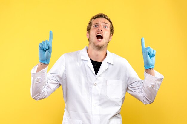 Vista frontale giovane medico maschio su sfondo giallo pandemia medica covid umana