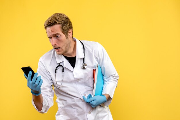 Vista frontale giovane medico maschio tenendo il telefono su sfondo giallo virus salute medico umano