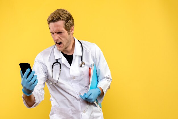 Vista frontale giovane medico maschio tenendo il telefono su sfondo giallo virus salute medico umano