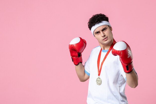 Vista frontale giovane pugile maschio in abbigliamento sportivo con guantoni da boxe sulla parete rosa
