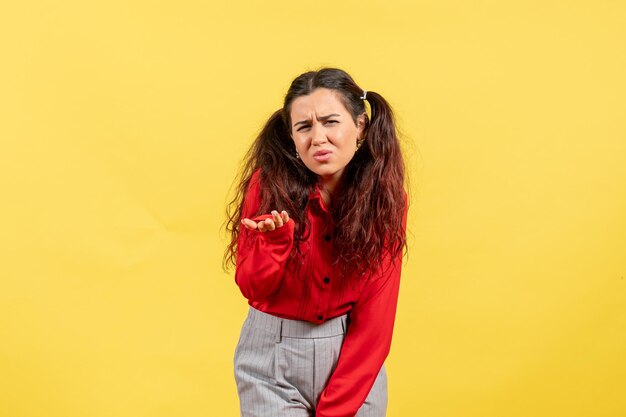 Vista frontale giovane ragazza in camicetta rossa con capelli carini e faccia confusa su sfondo giallo bambino bambino ragazza gioventù innocenza colore