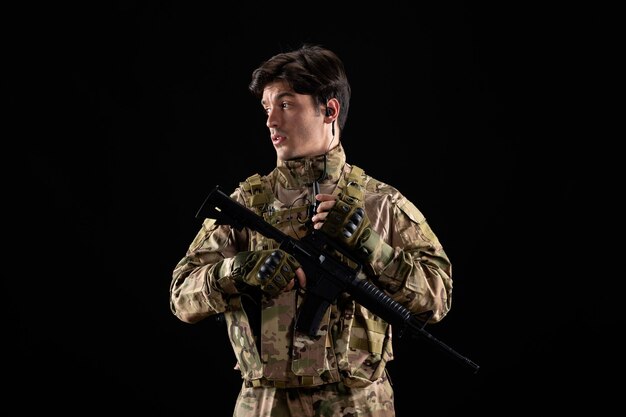 Vista frontale giovane soldato in uniforme durante il funzionamento sul muro nero