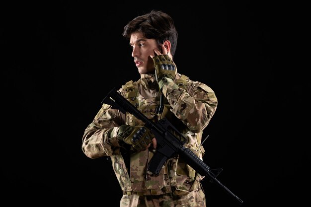 Vista frontale giovane soldato in uniforme durante il funzionamento sul muro nero