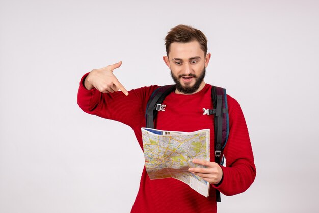 Vista frontale giovane turista maschio con zaino esplorando la mappa sul turismo di colore umano di colore umano di viaggio aereo città vacanza emozione