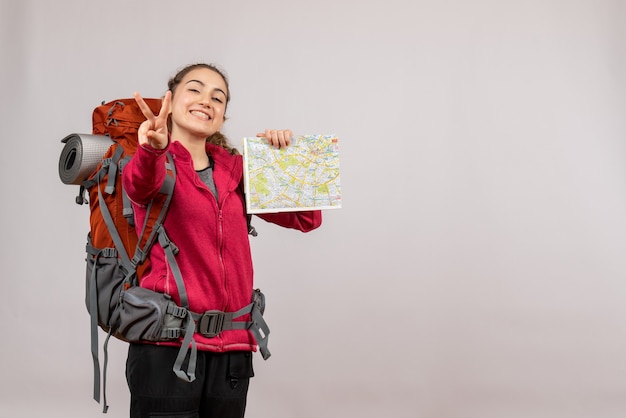 Vista frontale giovane viaggiatore con grande zaino in possesso di mappa che fa segno ok