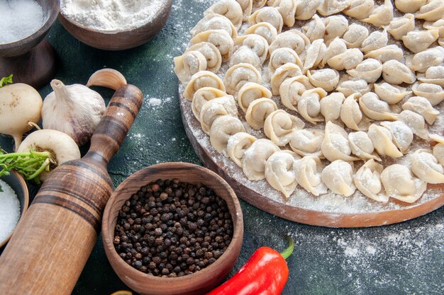 Vista frontale gnocchi crudi con farina e verdure su superficie scura