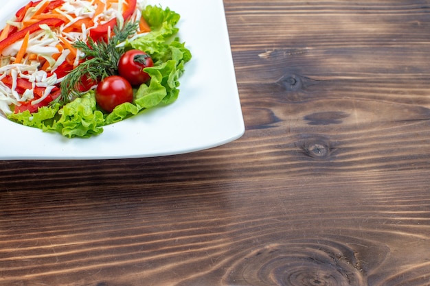 Vista frontale gustosa insalata di verdure con insalata verde e cavolo all'interno della piastra sulla superficie marrone