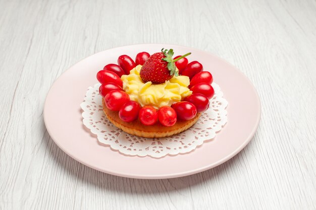 Vista frontale gustosa torta alla crema con cornioli su una scrivania bianca torta dessert frutta rossa
