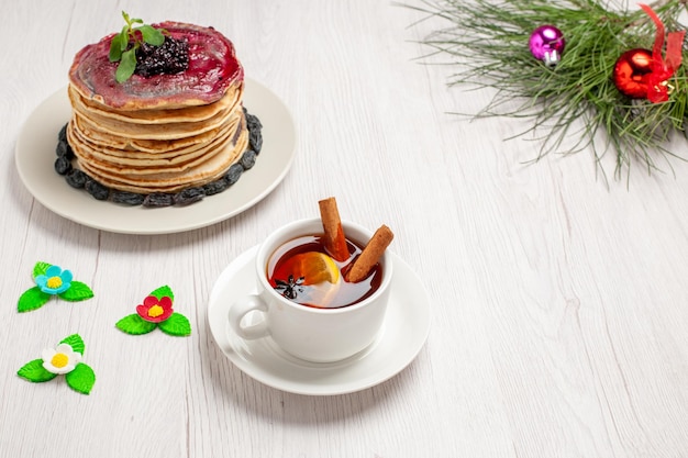 Vista frontale gustose frittelle di gelatina con gelatina fruttata di uvetta e tazza di tè su spazio bianco