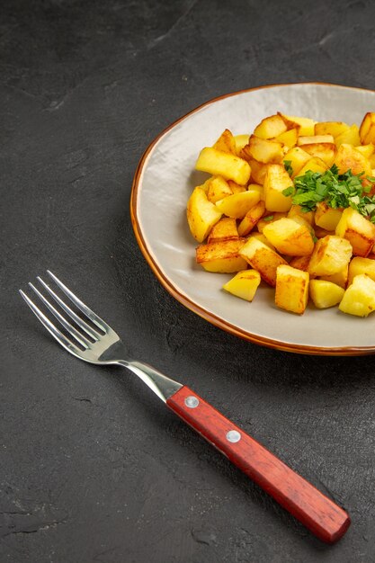 Vista frontale gustose patate fritte all'interno del piatto con verdure sul tavolo scuro