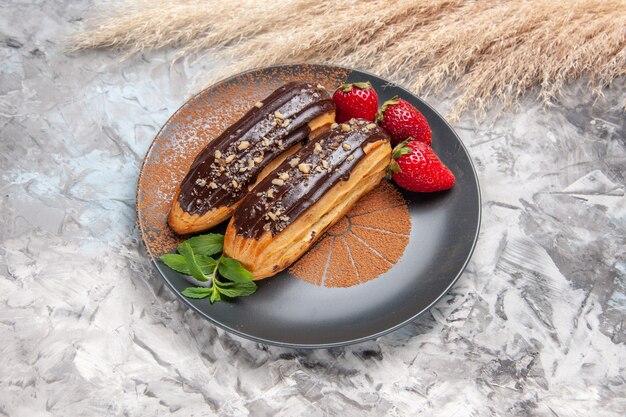 Vista frontale gustosi bignè al cioccolato con fragole su tavola leggera biscotti con biscotti dessert