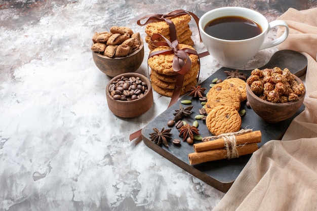 Vista frontale gustosi biscotti dolci con semi di caffè e tazza di caffè su sfondo chiaro zucchero cacao tè biscotto torta dolce torta