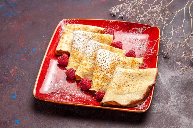 Vista frontale gustosi pancake dolci all'interno del piatto rosso con lamponi su spazio scuro