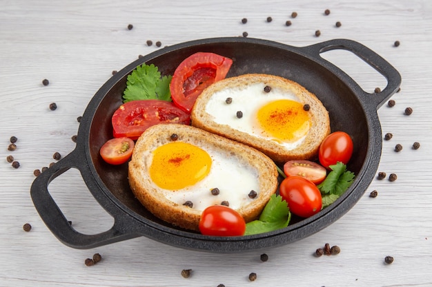 Vista frontale gustosi toast all'uovo con pomodori all'interno della padella su sfondo bianco colazione pranzo colore insalata cibo pasto
