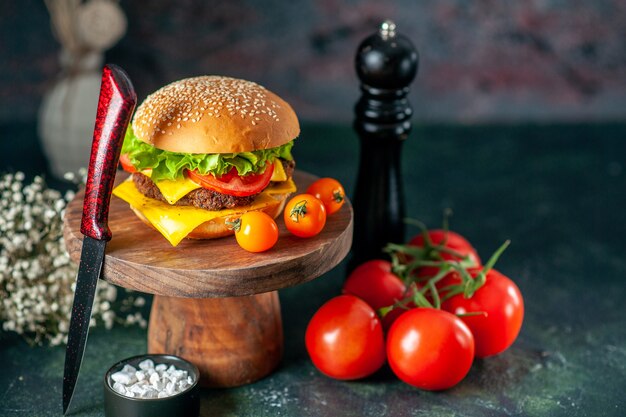 vista frontale gustoso hamburger di carne con pomodori coltello e agitatore di pepe su sfondo scuro