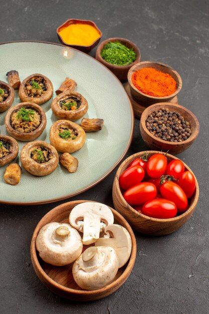 Vista frontale gustoso pasto a base di funghi con pomodori freschi e condimenti su un piatto da scrivania scuro cena a base di funghi