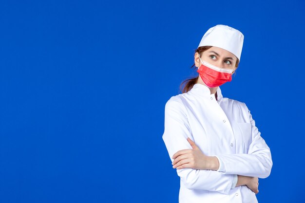 Vista frontale in posa giovane infermiera in tuta medica con maschera rossa sull'azzurro