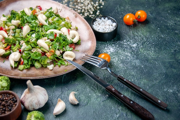 vista frontale insalata di verdure all'interno di un piatto elegante con posate su uno sfondo blu scuro