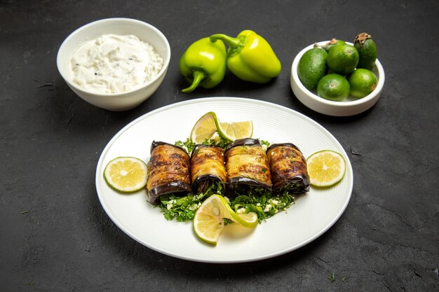 Vista frontale involtini salati di melanzane piatto cotto con fette di limone e feijoa su superficie scura olio per cena piatto da cucina