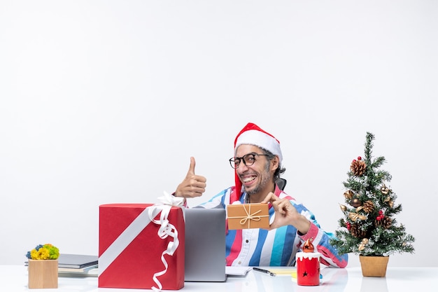 Vista frontale lavoratore di sesso maschile seduto nel suo posto di lavoro in possesso di pacchetto vacanze emozioni ufficio lavoro di natale