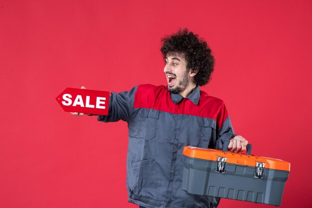 Vista frontale lavoratore maschio con valigetta degli attrezzi e targhetta di vendita su sfondo rosso meccanico foto uniforme strumento colore lavoro lavoratore