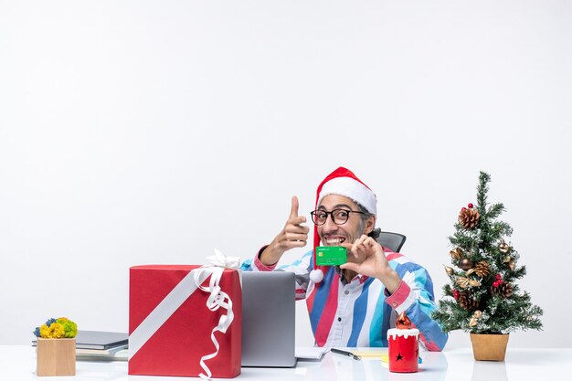 Vista frontale lavoratore maschio seduto nel suo posto di lavoro con in mano una carta di credito verde lavoro soldi emozione di natale