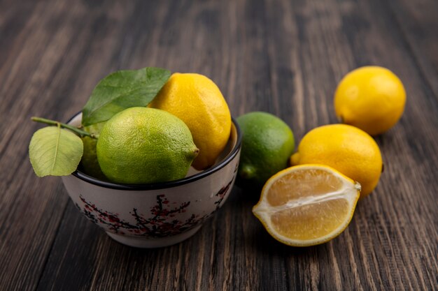 Vista frontale limette con limoni in una ciotola su sfondo di legno