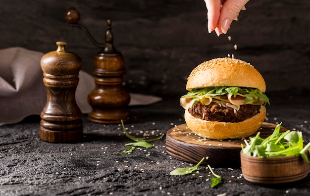 Vista frontale mano versando i semi di sesamo su hamburger di manzo con insalata e pancetta