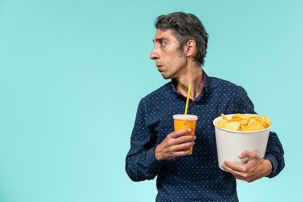 Vista frontale maschio di mezza età che tiene patatine fritte e soda sulla superficie blu