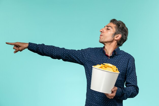 Vista frontale maschio di mezza età che tiene patatine fritte sulla superficie blu