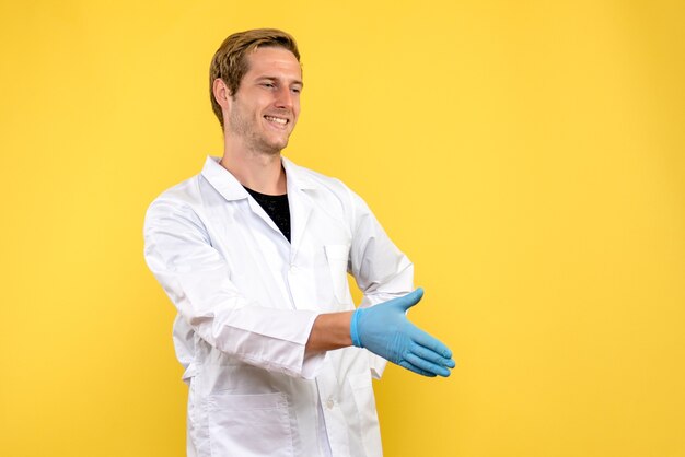 Vista frontale maschio medico stringe la mano su sfondo giallo salute medico covid-pandemia