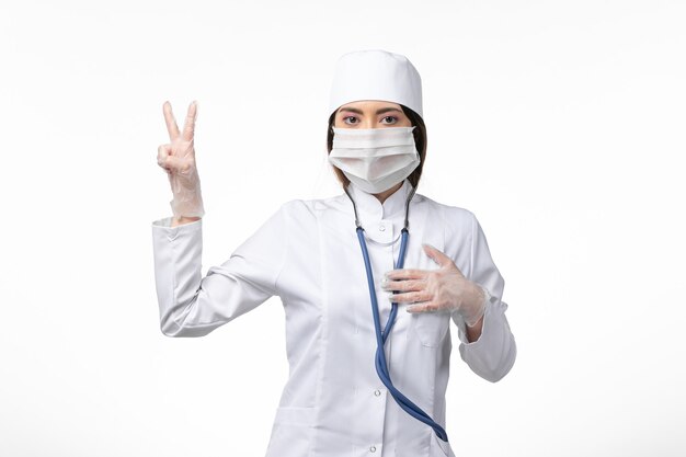 Vista frontale medico donna in tuta medica bianca con una maschera a causa di una pandemia sul muro di luce medicina virus pandemico covid-