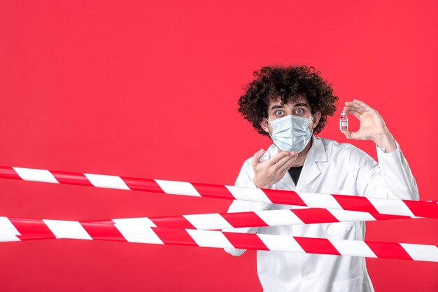 Vista frontale medico maschio che tiene fiaschetta con medicina su sfondo rosso uniforme covid- salute colore pericolo medico quarantena