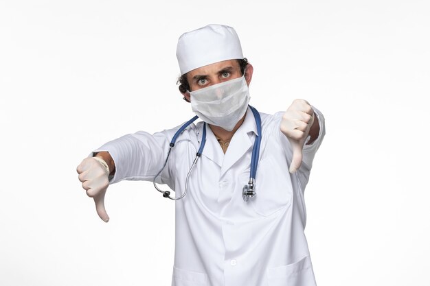 Vista frontale medico maschio in tuta medica che indossa una maschera sterile come protezione dalla pandemia covid-on white wall virus covid
