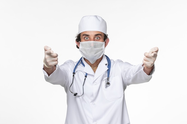 Vista frontale medico maschio in tuta medica che indossa una maschera sterile come protezione dalla pandemia del coronavirus del virus della spruzzata del muro bianco covid