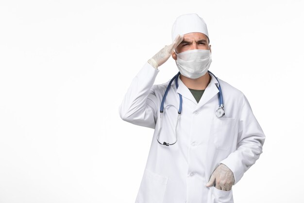 Vista frontale medico maschio in tuta medica e indossa una maschera a causa di covid- sulla parete bianca chiara covid- virus pandemico malattia da virus