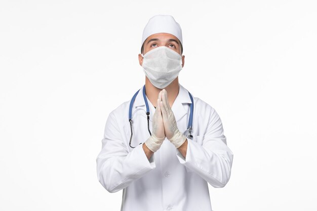 Vista frontale medico maschio in tuta medica e indossa una maschera contro covid pregando sul muro bianco virus covid- malattia pandemia malattia