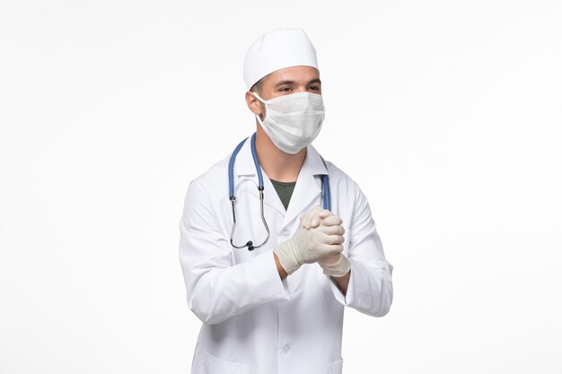 Vista frontale medico maschio in tuta medica e indossa una maschera contro covid sul muro bianco chiaro virus covid - malattia pandemia malattia
