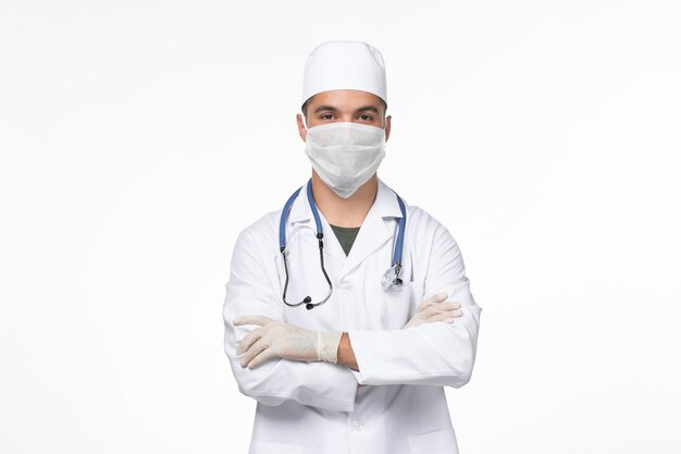Vista frontale medico maschio in tuta medica e indossa una maschera contro covid sul muro bianco virus covid- malattia pandemia malattia