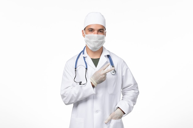 Vista frontale medico maschio in tuta medica e maschera da indossare a causa di covid- in posa sul muro bianco malattia virus covid- malattia pandemica