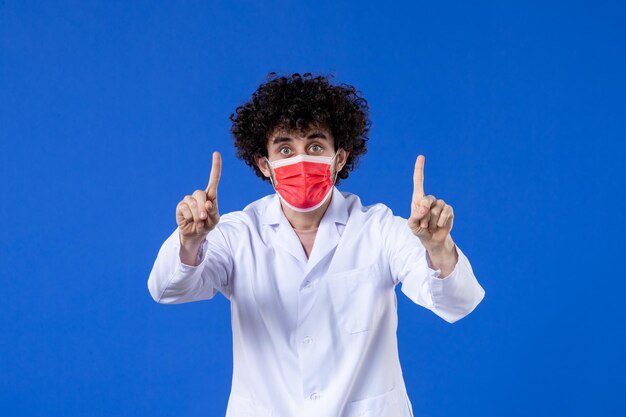 Vista frontale medico maschio in tuta medica e maschera su sfondo blu vaccino farmaco ospedale covid-virus della medicina sanitaria