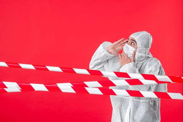 Vista frontale medico maschio in tuta protettiva e maschera su sfondo rosso isolamento virus covid-cura ospedale colore quarantena