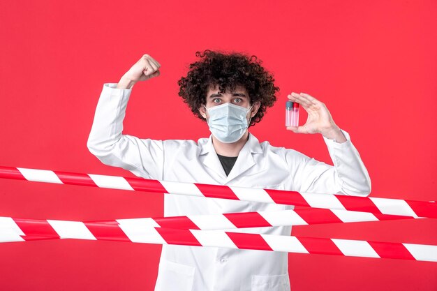 Vista frontale medico maschio in uniforme medica che tiene flaconi su sfondo rosso colore covid- pericolo per la salute avvertenza isolamento quarantena