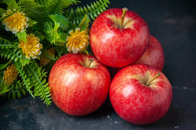 Vista frontale mele rosse fresche con pianta verde su uno sfondo scuro colore dolce pera cibo maturo vitamina dieta mela
