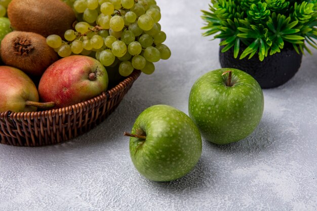 Vista frontale mele verdi con pera uva verde e kiwi in un cesto su uno sfondo bianco