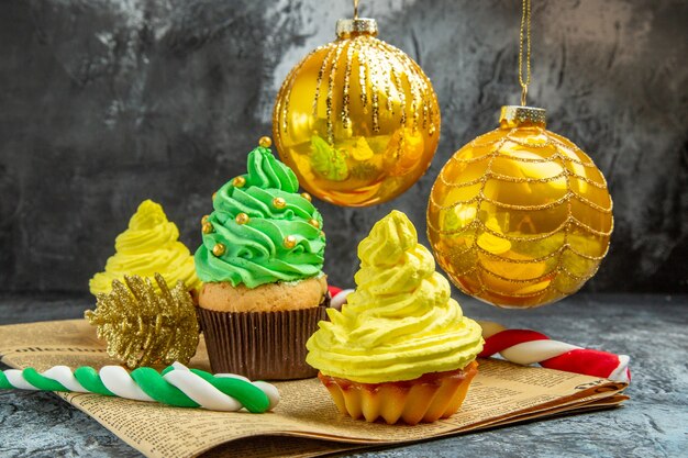 Vista frontale mini cupcakes colorati albero di natale giocattoli e caramelle sul giornale su foto di capodanno scuro