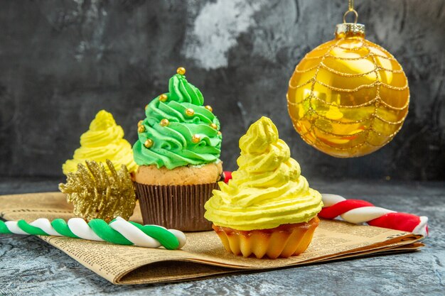 Vista frontale mini cupcakes colorati albero di natale giocattolo caramelle di natale sul giornale su sfondo scuro