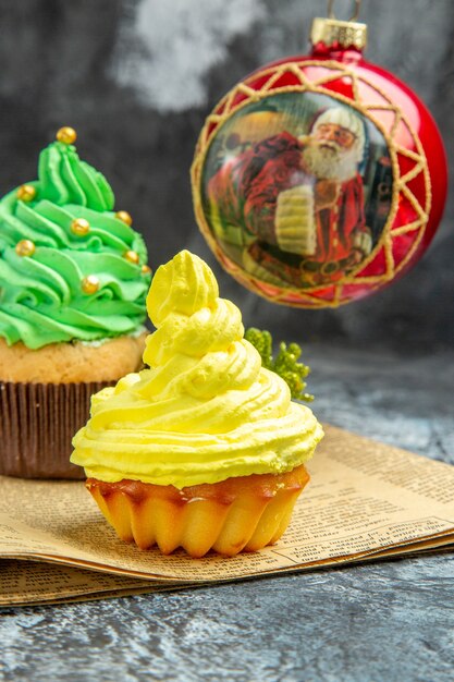 Vista frontale mini cupcakes colorati palla rossa dell'albero di natale sul giornale sulla foto scura del nuovo anno