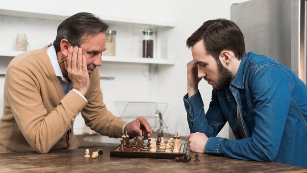 Vista frontale padre e figlio, giocare a scacchi in kithcen