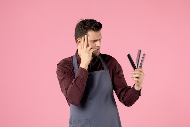 vista frontale parrucchiere maschio che tiene spazzole per capelli su sfondo rosa